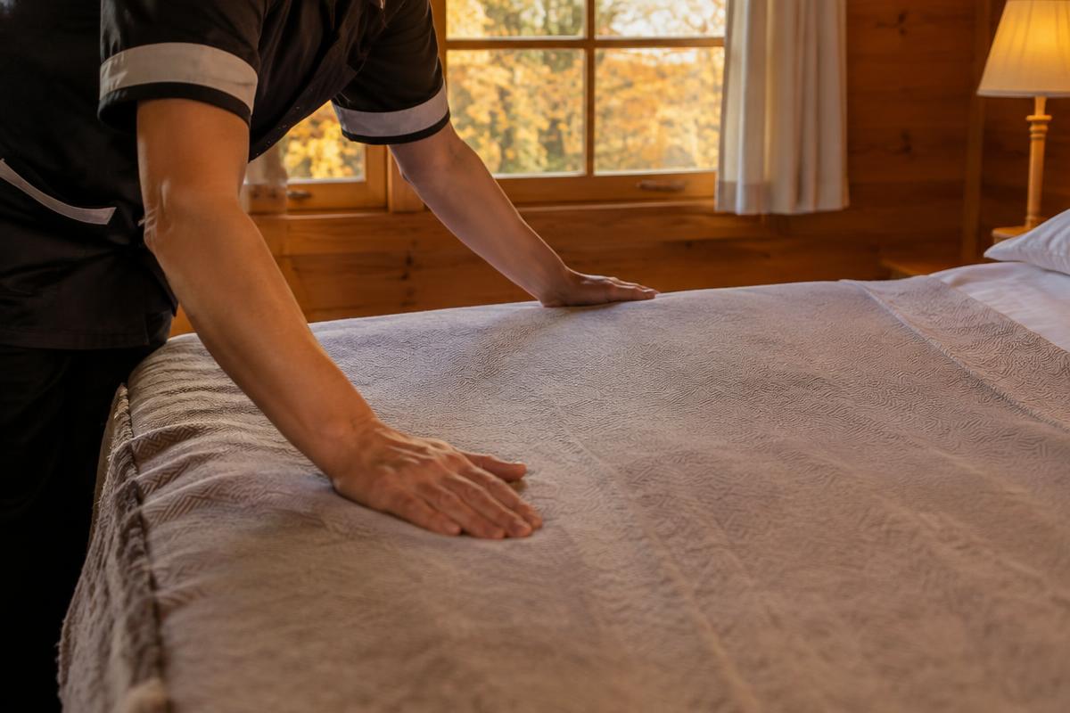 Hands smoothing a bedspread in a cabin bedroom in fall light